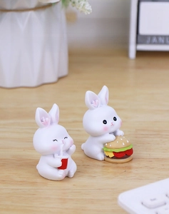 Detail of two mini resin rabbit figurines eating burger and drinking on a wooden desk