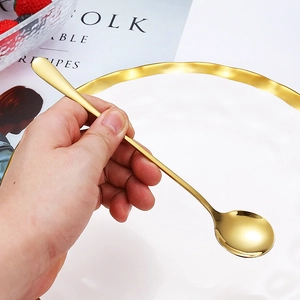 Golden stainless steel long handle mixing spoon held by hand over a white plate and book