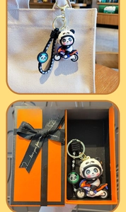 Dettaglio portachiavi panda in moto con cinturino intrecciato e scatola regalo arancione