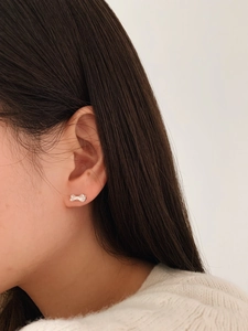 Close-up of a silver bow stud earring worn on the ear to show size and sweet style
