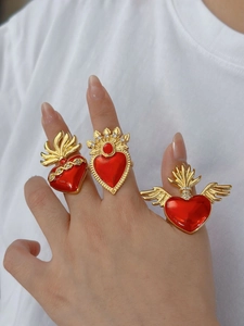Detailed view of three gold-tone sacred heart rings with red enamel wings and rhinestones