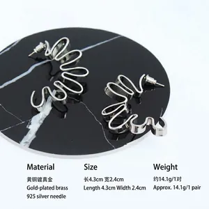 Abstract silver-colored wavy brass earrings with 925 silver needles on black marble base