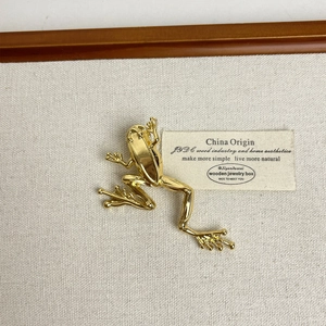 Detailed view of a golden frog brooch in polished metal on a minimalist background