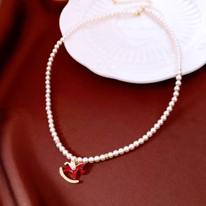 Detailed shot of a red horse pendant pearl necklace on a white embossed plate