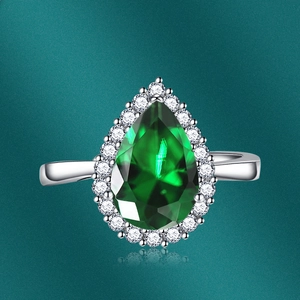 Macro shot of pear-cut emerald gemstone ring with diamond halo and silver band