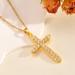 Nahaufnahme der goldenen Kreuzkette mit Kristallen auf Marmor und beigem Stoff