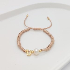 Detail of handmade woven bracelet featuring white pearl and gold metal letter U charm