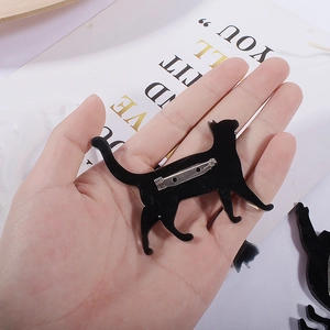 Handheld view of a glossy black acrylic cat brooch with a sturdy silver metal pin back