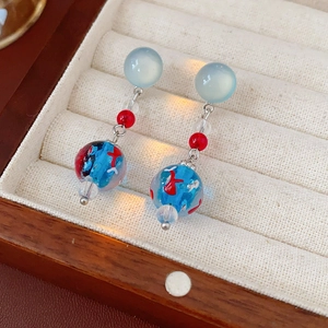 Macro detail of starfish earrings with blue glass beads and fish motif in a wooden box