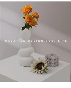 Detail view of white ceramic pebble vase with orange roses and soft window lighting