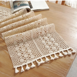 Beige crochet table runner with lace patterns and tassels on a wooden dining table