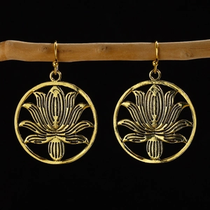Golden lotus patterned circular earrings hanging on a wooden branch against black backdrop