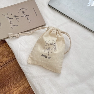 Close-up of cream canvas drawstring pouch with artistic face line drawing for travel storage