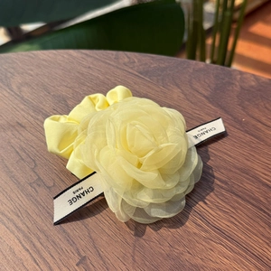 Yellow organza rose hair clip with ribbon detail on a dark wooden background