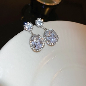 Macro detail of silver needle earrings featuring sparkling zircon halo and oval drop pendant