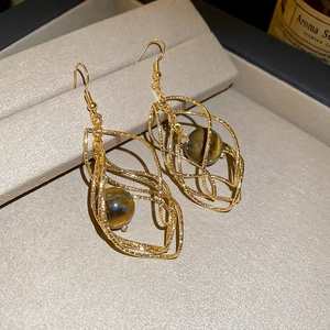 Macro detail of golden hollow spiral cage earrings with brown tiger eye stone beads
