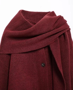 Dettaglio del collo alto e del bottone nero su un maglione poncho a maglia bordeaux