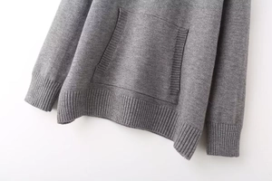 Detail of ribbed cuffs, hem, and front pocket on a grey knitted oversized hoodie