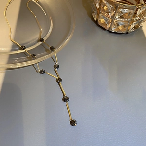 Close-up of golden Y-shaped long necklace with faceted black beads on a textured surface