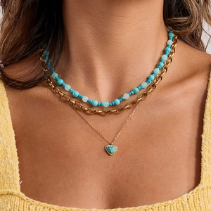 Three-layer gold chain necklace with turquoise beads and heart pendant on a model