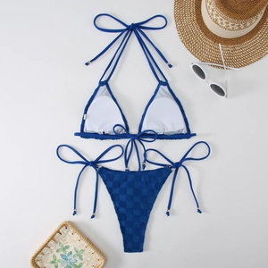 Flat lay of navy blue checkered bikini set with neck ties and summer beach accessories
