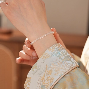 Detailed macro view of clear white crystal beaded bracelet worn on wrist with blue silk shirt