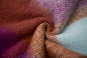 Macro view of soft thick plaid scarf texture showing purple and orange woven fibers