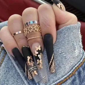 Detail of extra long matte black nails with gold butterfly patterns and rhinestones
