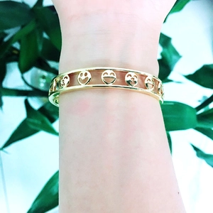 Detail of gold chunky chain bracelet featuring hollow smiling face design worn on wrist