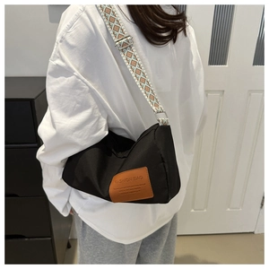 Detail of black nylon crossbody bag featuring a wide patterned strap and leather patch