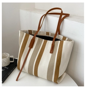 Detailed view of woven canvas tote bag with vertical stripes and brown leather straps