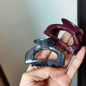 Close-up of dark purple and grey acetate hair claws with gold moliveny lettering
