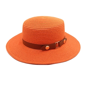 Detail of vibrant orange straw sun hat featuring brown leather band and gold metal buckle
