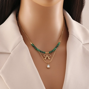 Double-layer gold necklace with green beads, bow charm, and crystal drop pendant