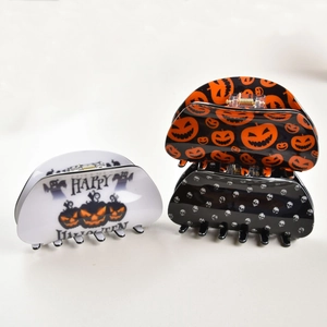 Detail view of Halloween hair claws featuring pumpkin and skull patterns on a grey background