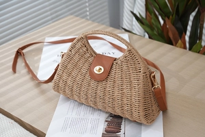 Close-up of woven straw bag texture with brown leather flap and gold twist lock clasp