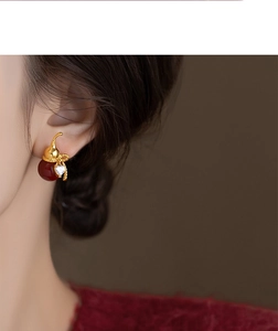 Detail of gold-plated gourd stud earring with red bead and heart zircon on model
