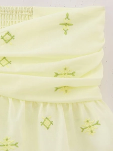 Détail du tissu jaune clair avec broderie d'étoiles vertes et volants plissés
