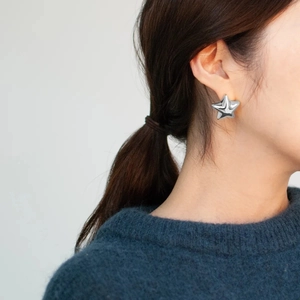 Close-up of a model wearing a polished silver star-shaped earring with a high-shine finish