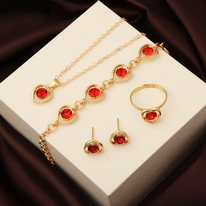 Close-up of golden four-piece jewelry set with red heart crystals on brown silk