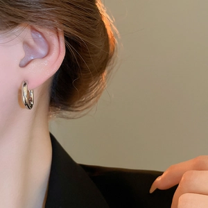Close-up of minimalist silver round hoop earring worn on ear with warm orange background