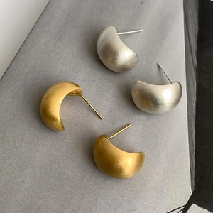 Detailed view of C-shaped metal stud earrings with brushed gold and silver finishes