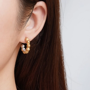 Vintage textured C-shape gold earrings with white pearls shown on a model ear