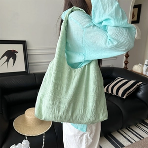 Detail of light green pleated tote bag with textured fabric shown on a model's shoulder