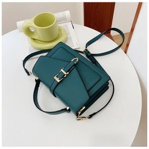 Detailed view of dark green PU leather crossbody bag with gold buckle on a white table