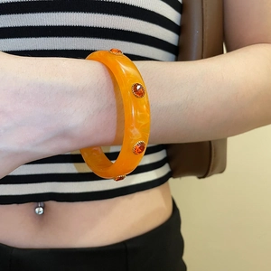 Detail of a bright orange acrylic cuff bracelet featuring crystal studs on model wrist