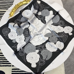 Elegant black and white camellia pattern square silk scarf displayed on a marble table