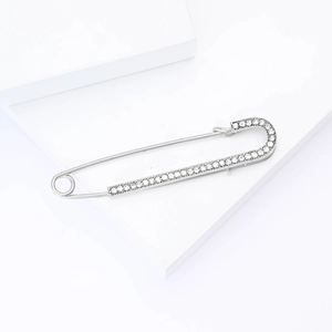 Close-up of a silver safety pin brooch with sparkling crystals on a white pedestal
