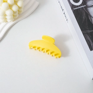 Detail of a vibrant yellow acetate hair claw clip in a stylish shell shape design
