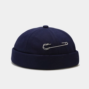 Detail of dark blue brimless docker cap featuring a large silver metal pin decoration